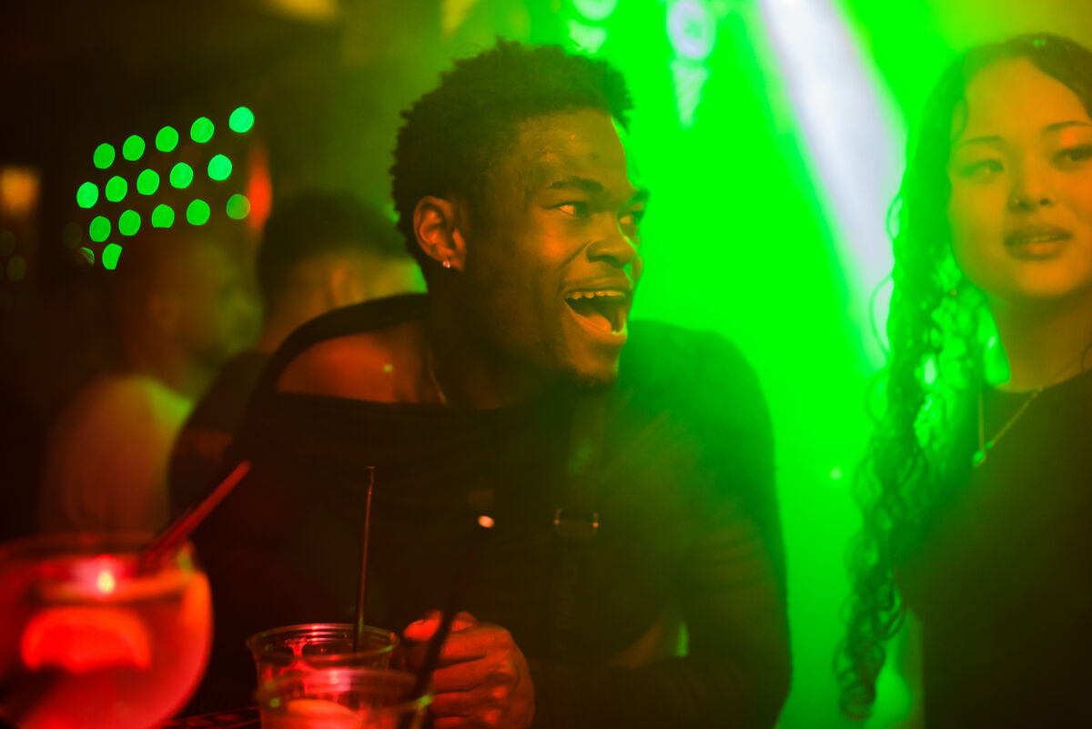 Guest laughing under green light with cocktails at Bar Blend Amsterdam