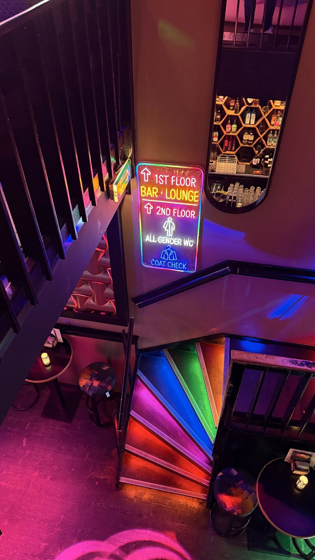 Rainbow-lit spiral staircase and a neon floor sign seen from above inside Bar Blend Amsterdam
