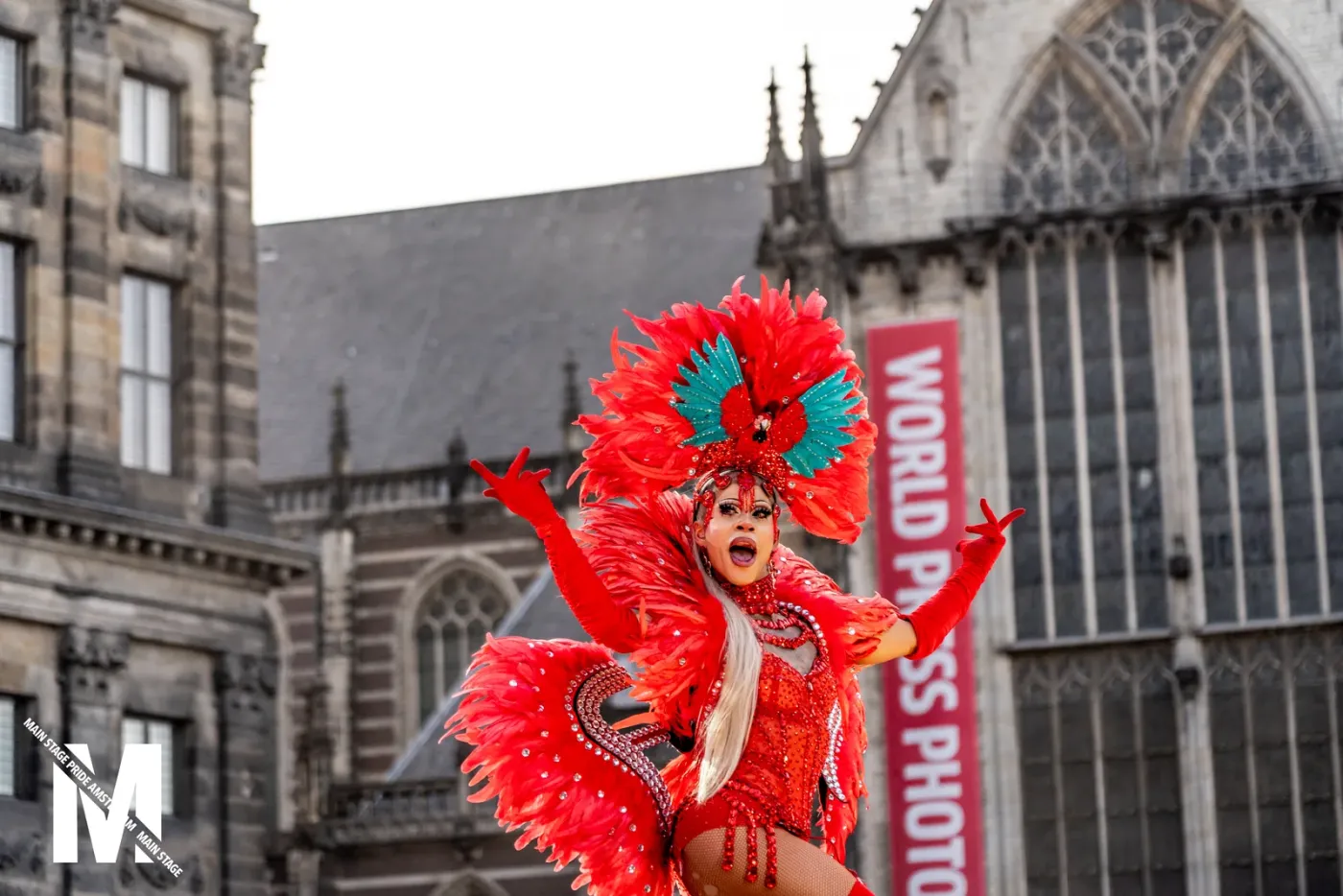 Performer in a red carnival feather costume in front of the Nieuwe Kerk during MainStage Pride Amsterdam