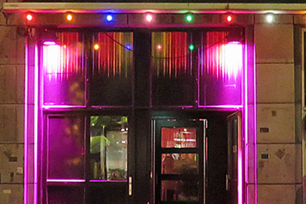The entrance of Café Montmartre XL on Reguliersdwarsstraat at night, with coloured bulbs along the awning and a red rope at the door
