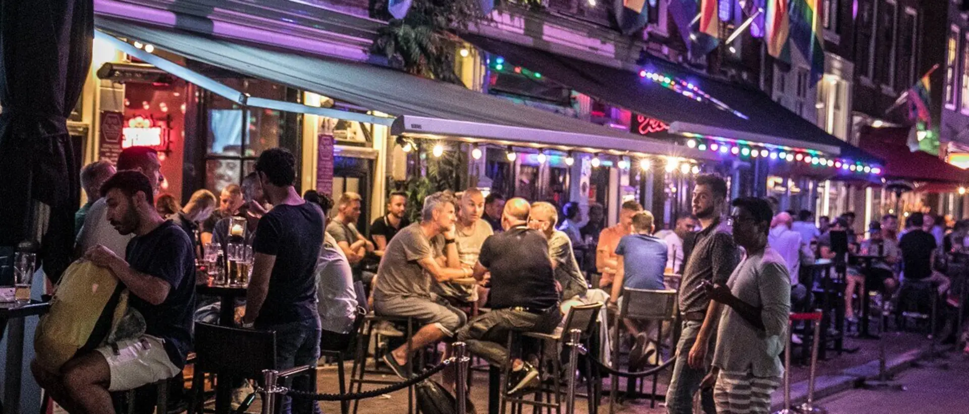 Volle terrassen op de Reguliersdwarsstraat op een zomeravond, met lichtjes onder de luifels