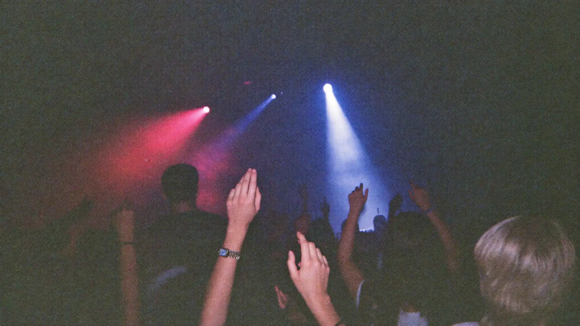 Hands in the air on a packed dance floor in blue and magenta light