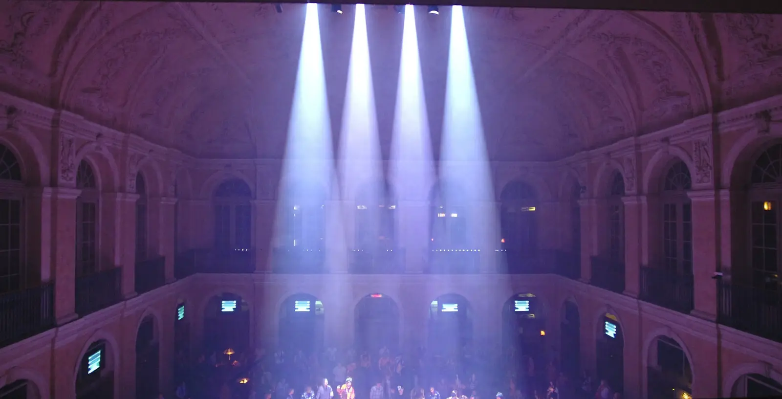 A nineteenth-century hall with light beams above a dancing crowd