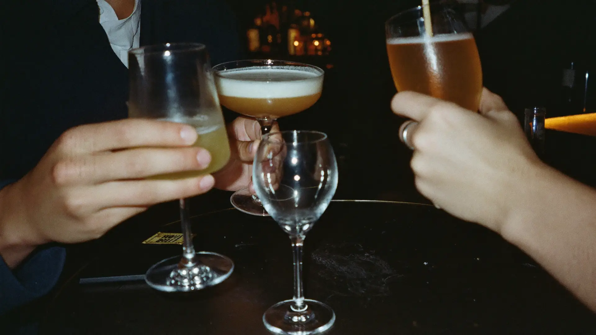 Friends toasting with a cocktail, beer and wine at a bar table