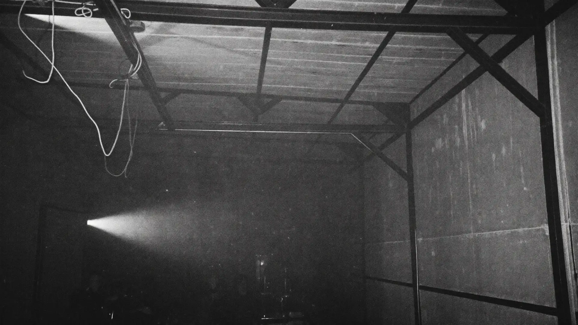 A bare concrete club space with haze and a single white light, in black and white