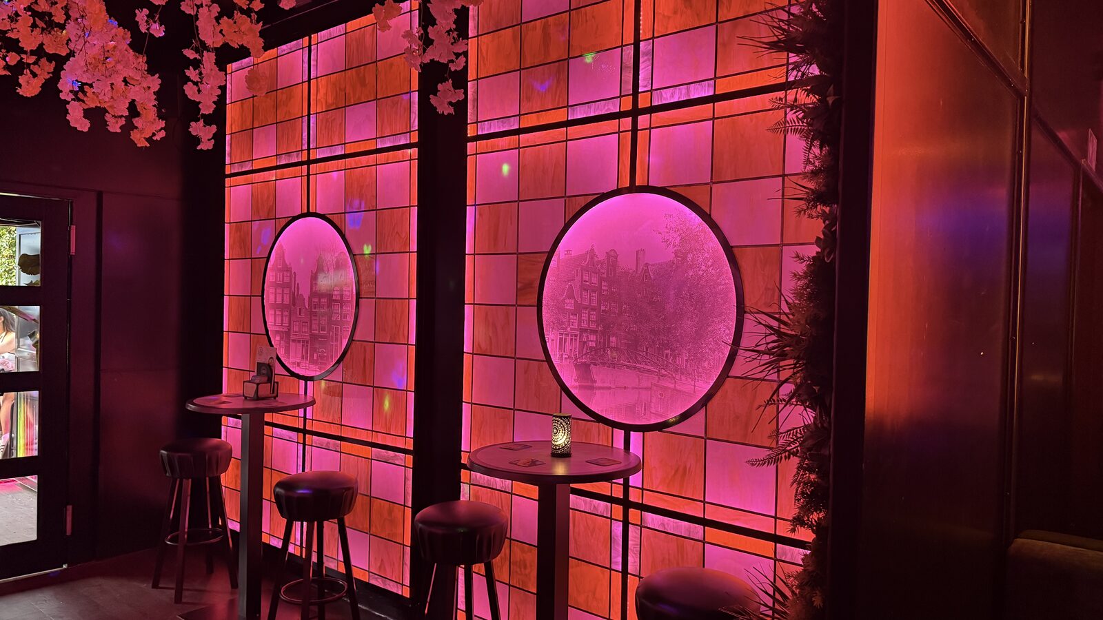 Pink-lit backlit panels and bar stools along the tiled wall inside Montmartre XL in Amsterdam